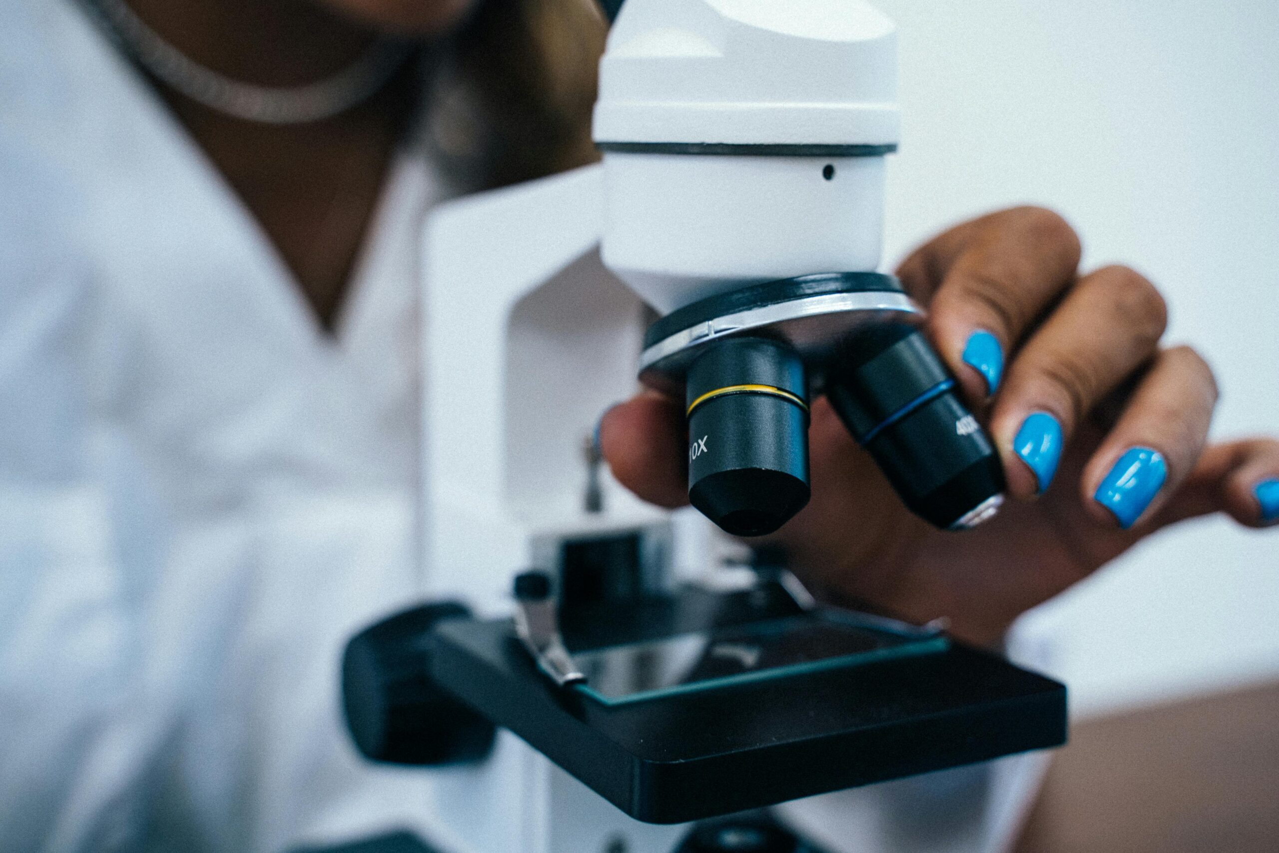 Close-up of a scientist's hand adjusting a microscope in a laboratory setting.